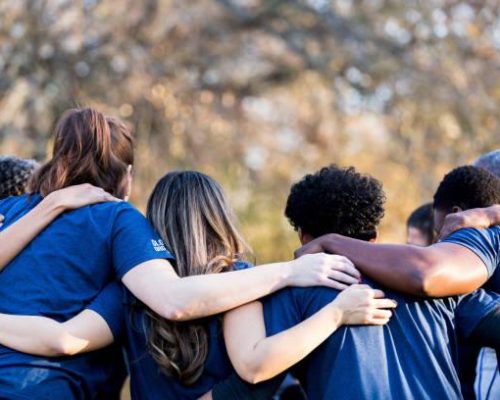 Diverse group of friends cleanup a park during a charity event. They are standing with their arms around one another.